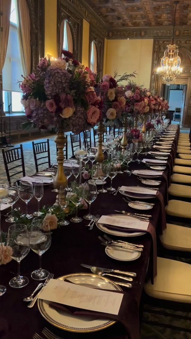 Deep purple banquet table with lavender and purple floral centerpieces in gold vases.