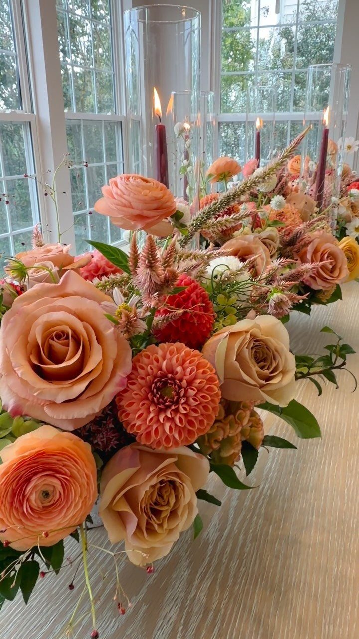 Dusty rose and peach floral centerpiece with burgundy taper candles on a table.
