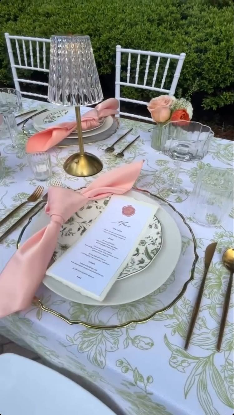 Outdoor table setting with peach napkins and green leaf patterned tablecloth and white plates.