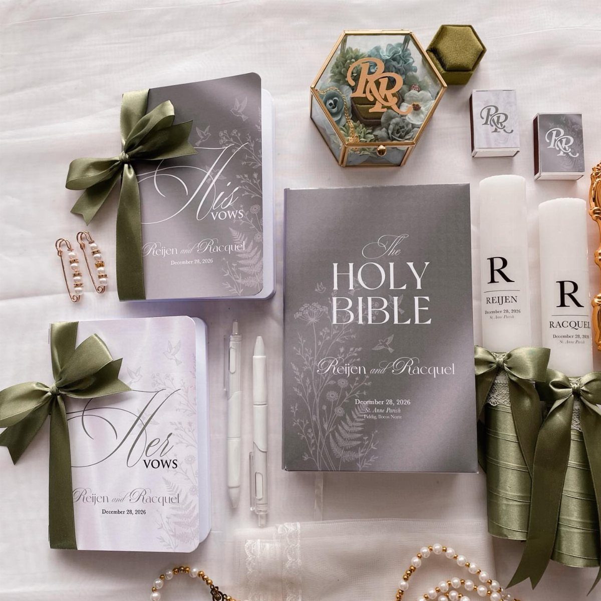 Wedding accessories including a Bible and vow books with sage green ribbons on white fabric.