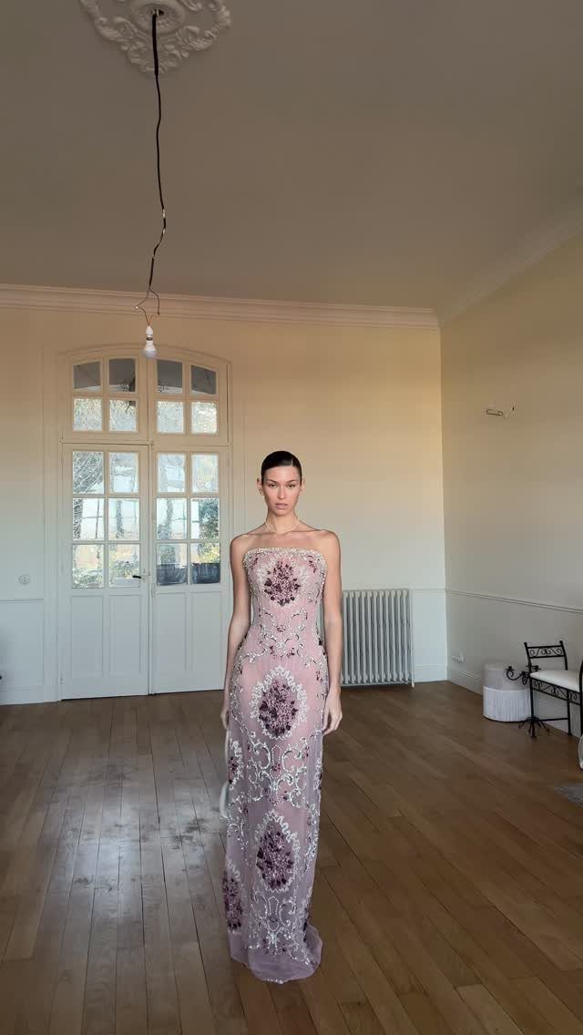 Woman in a strapless mauve floral embroidered gown standing in a bright room.