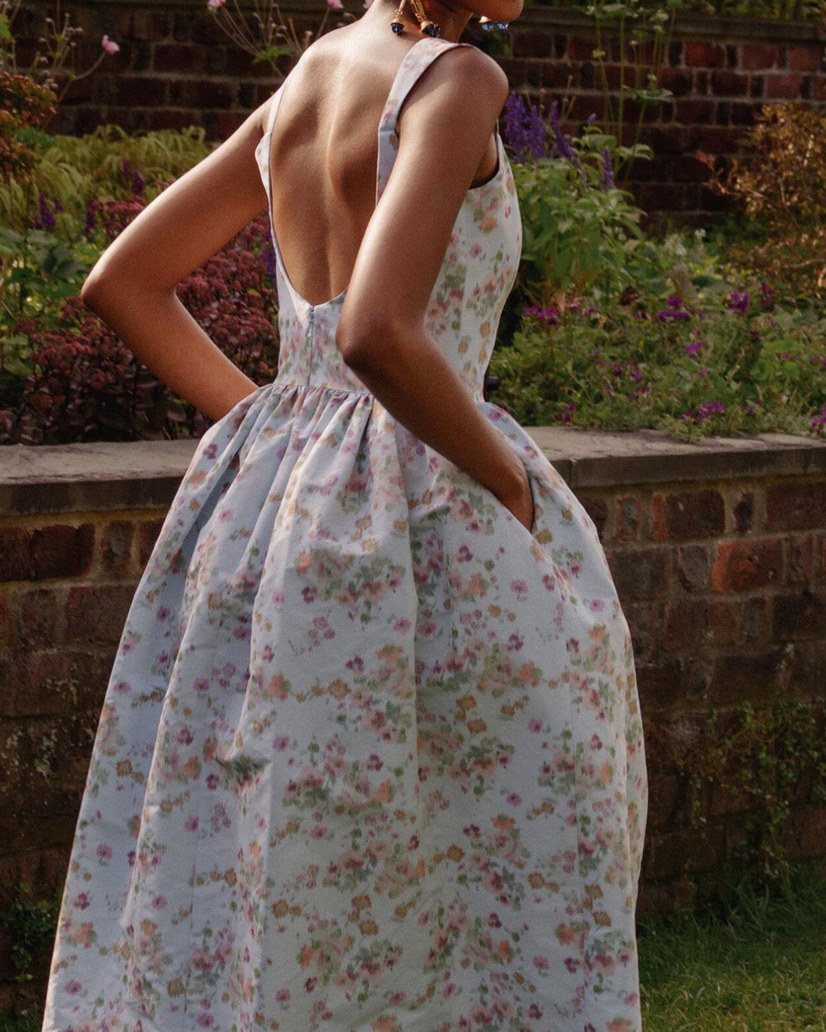 Woman in a light blue floral maxi dress standing in a lush garden.