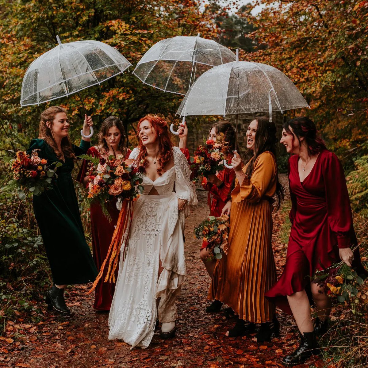 Bride and bridesmaids in rich autumn colored dresses standing in a fall forest.