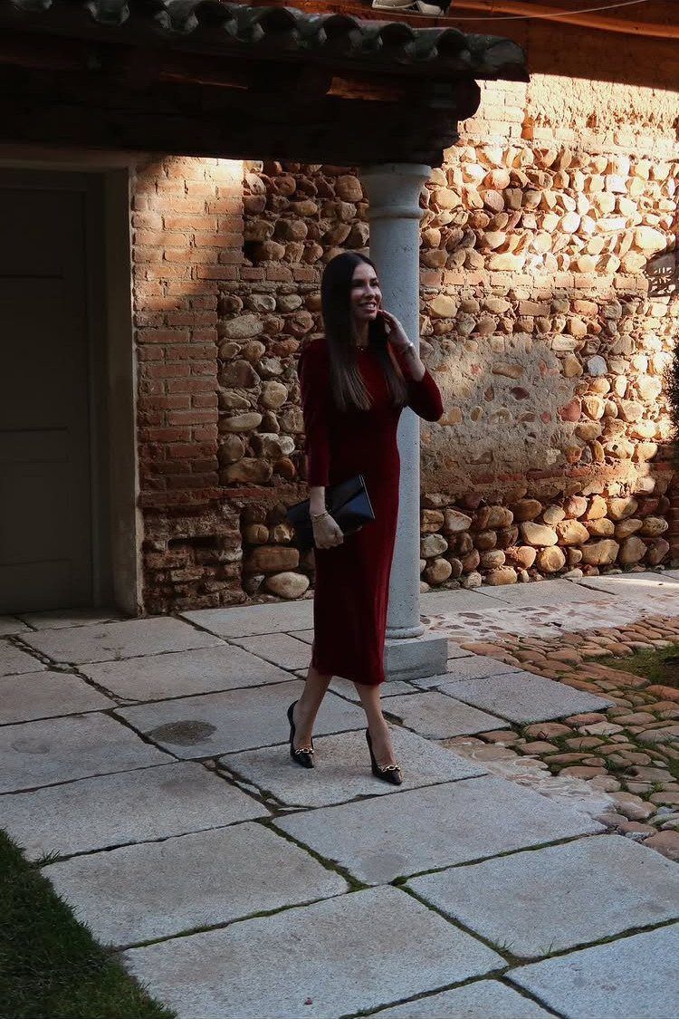 Woman in a dark red velvet midi dress and black heels on a stone patio.