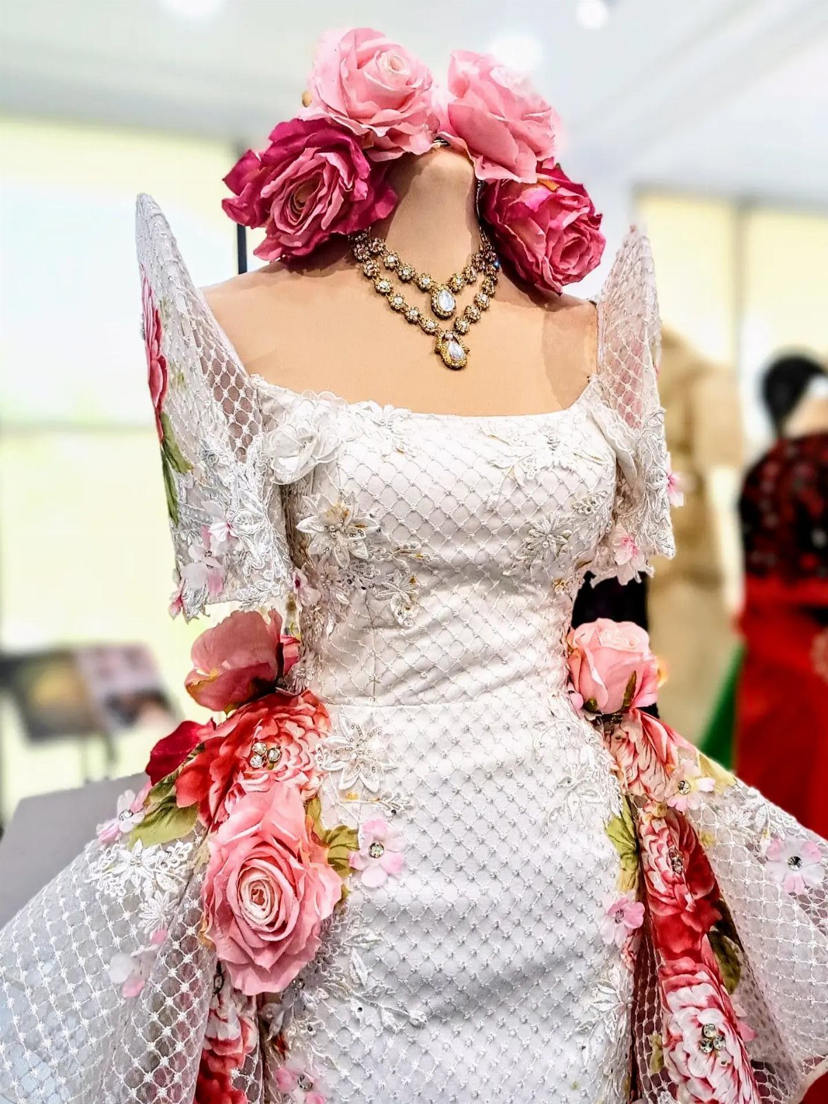 White Filipiniana dress with butterfly sleeves and pink floral accents on a mannequin.