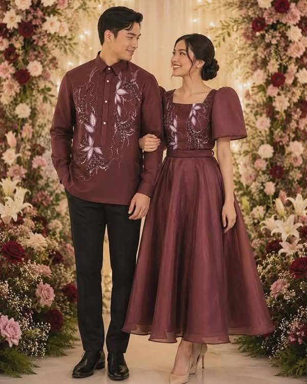 Couple wearing maroon traditional Filipino wedding attire posing before a floral wall.