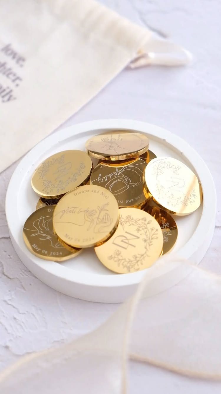 Gold wedding coins with engravings resting in a small white ceramic dish.