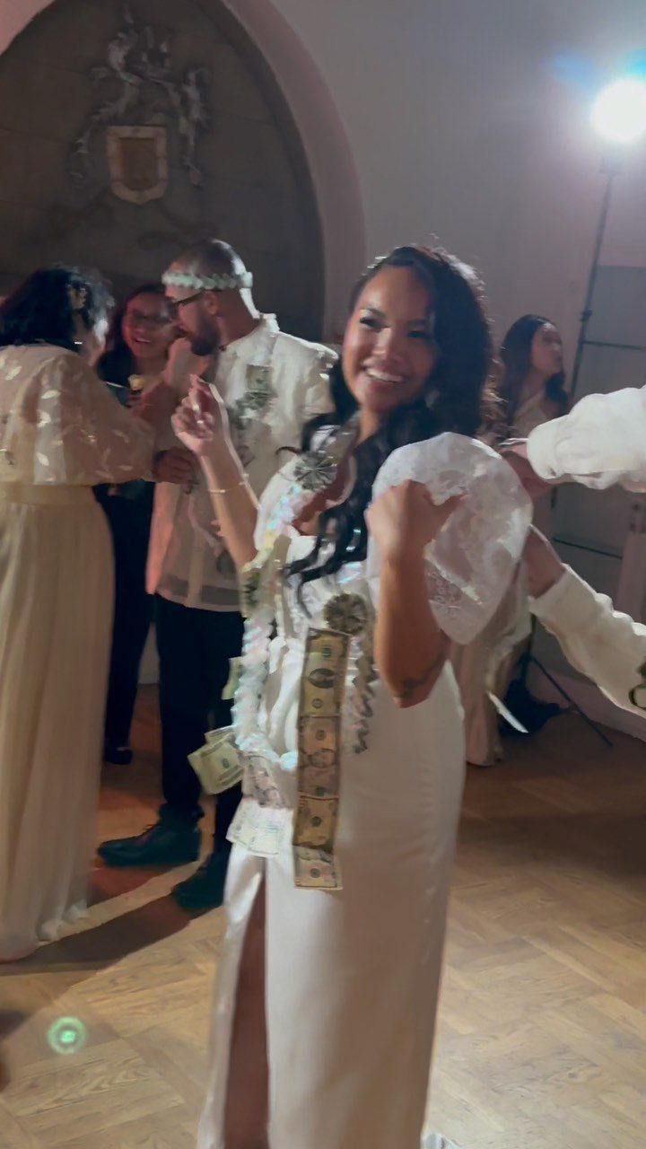 Woman in white Filipiniana gown with money bills pinned to her dress during wedding.