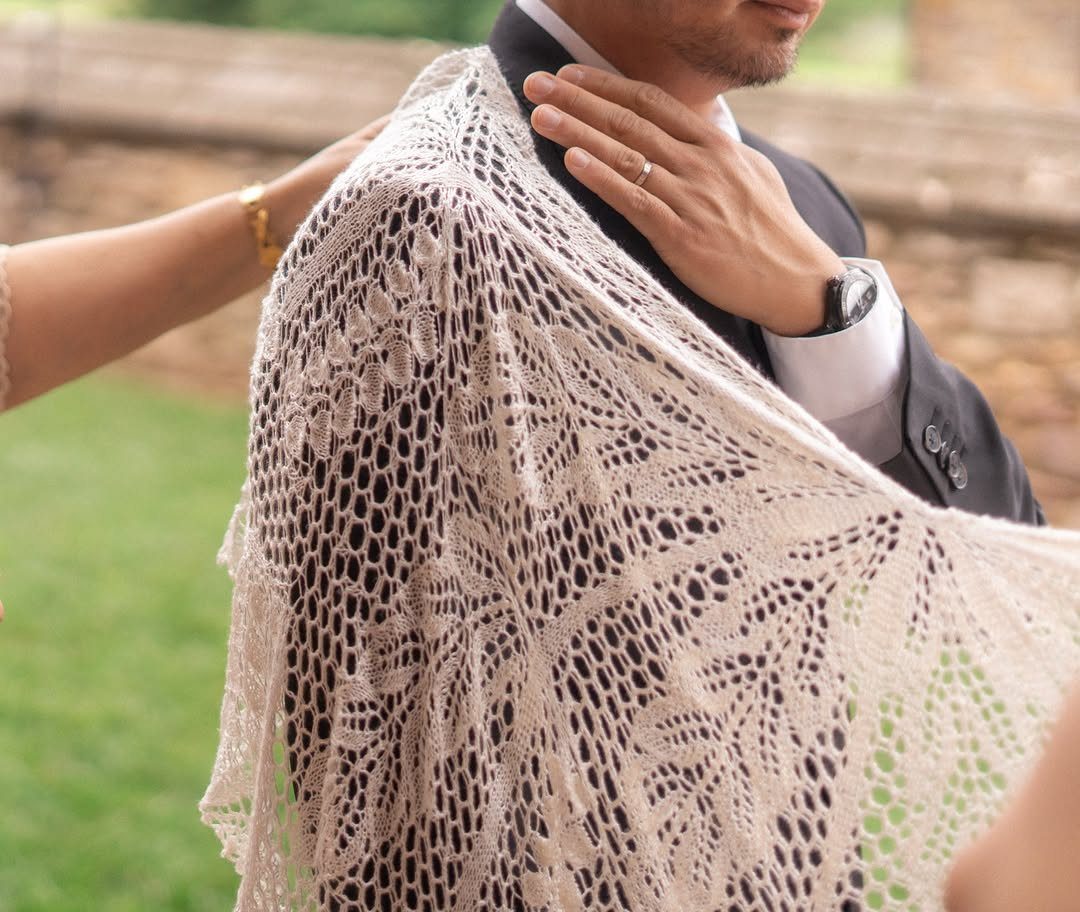 Lace wedding veil being draped over the shoulder of a groom in a suit.