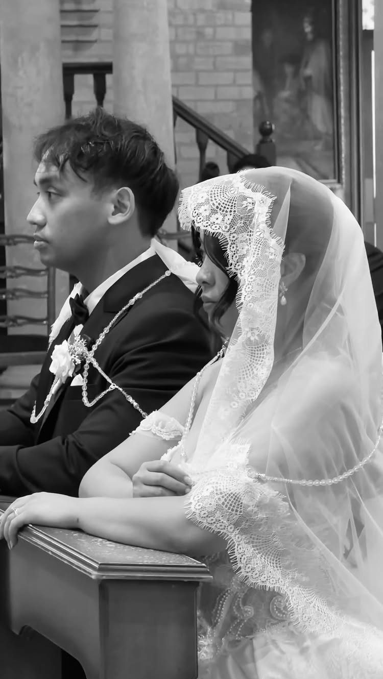Bride and groom in a church with a ceremonial wedding cord draped over them.