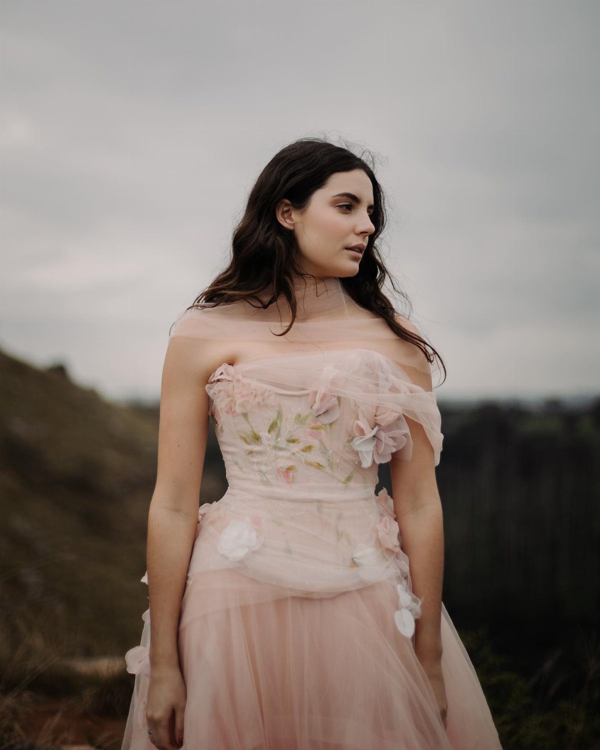 Woman in a pink floral tulle wedding dress standing in a hilly landscape