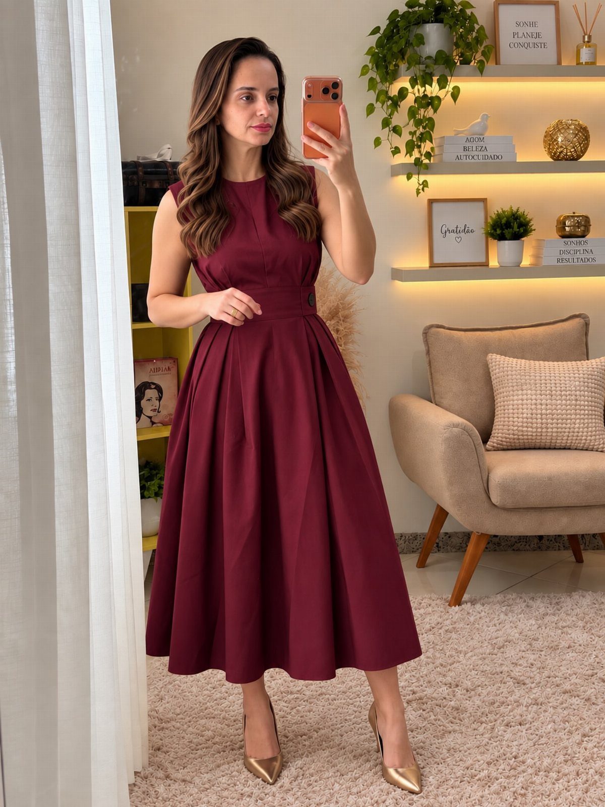 Woman wearing a sleeveless burgundy midi dress and gold heels in a living room.