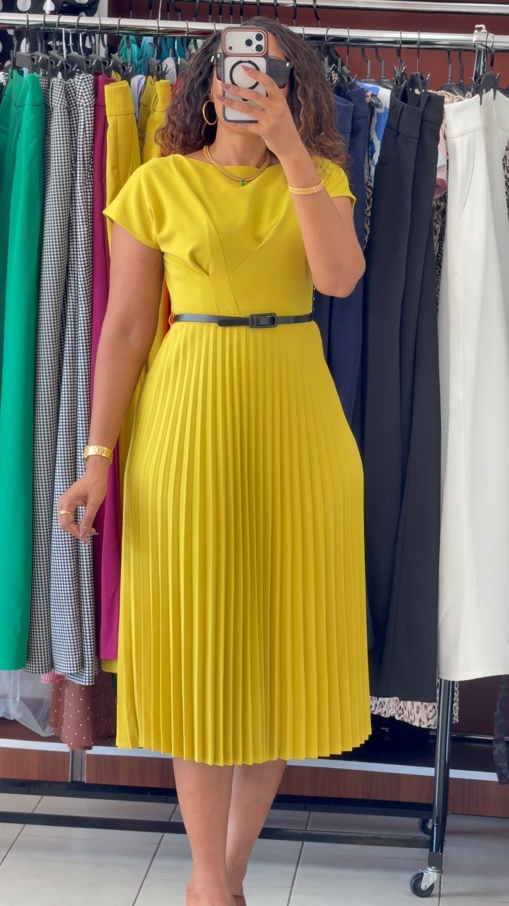 Woman in a yellow midi dress with a pleated skirt and black belt.