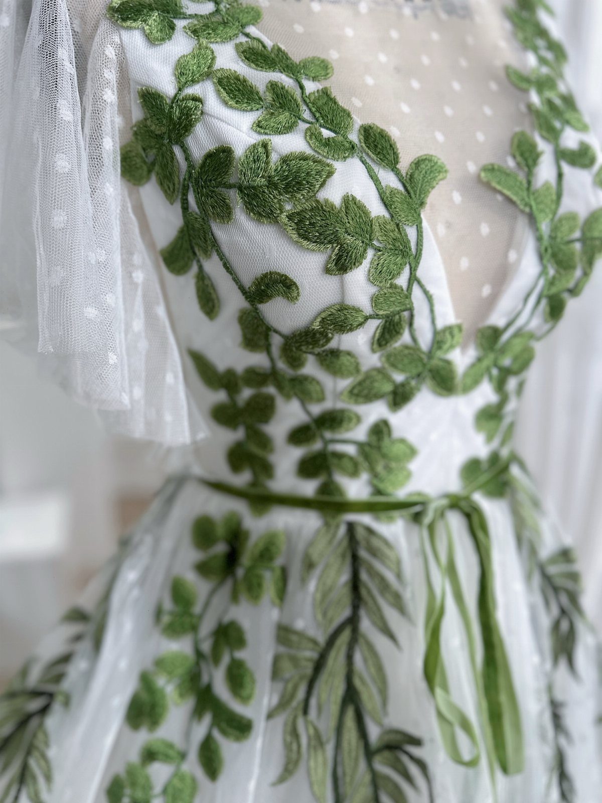 White wedding dress with green leaf embroidery and a green ribbon waist belt.