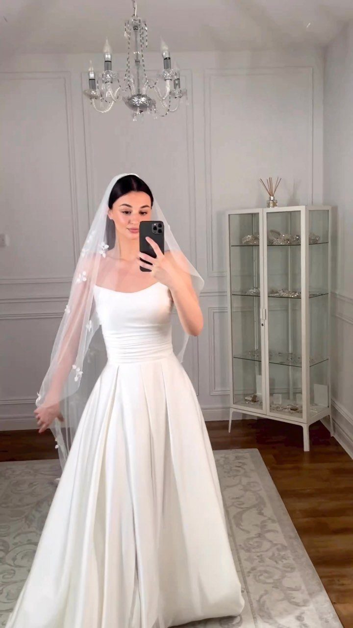 Woman in a strapless white A-line wedding dress and embroidered veil taking a selfie.