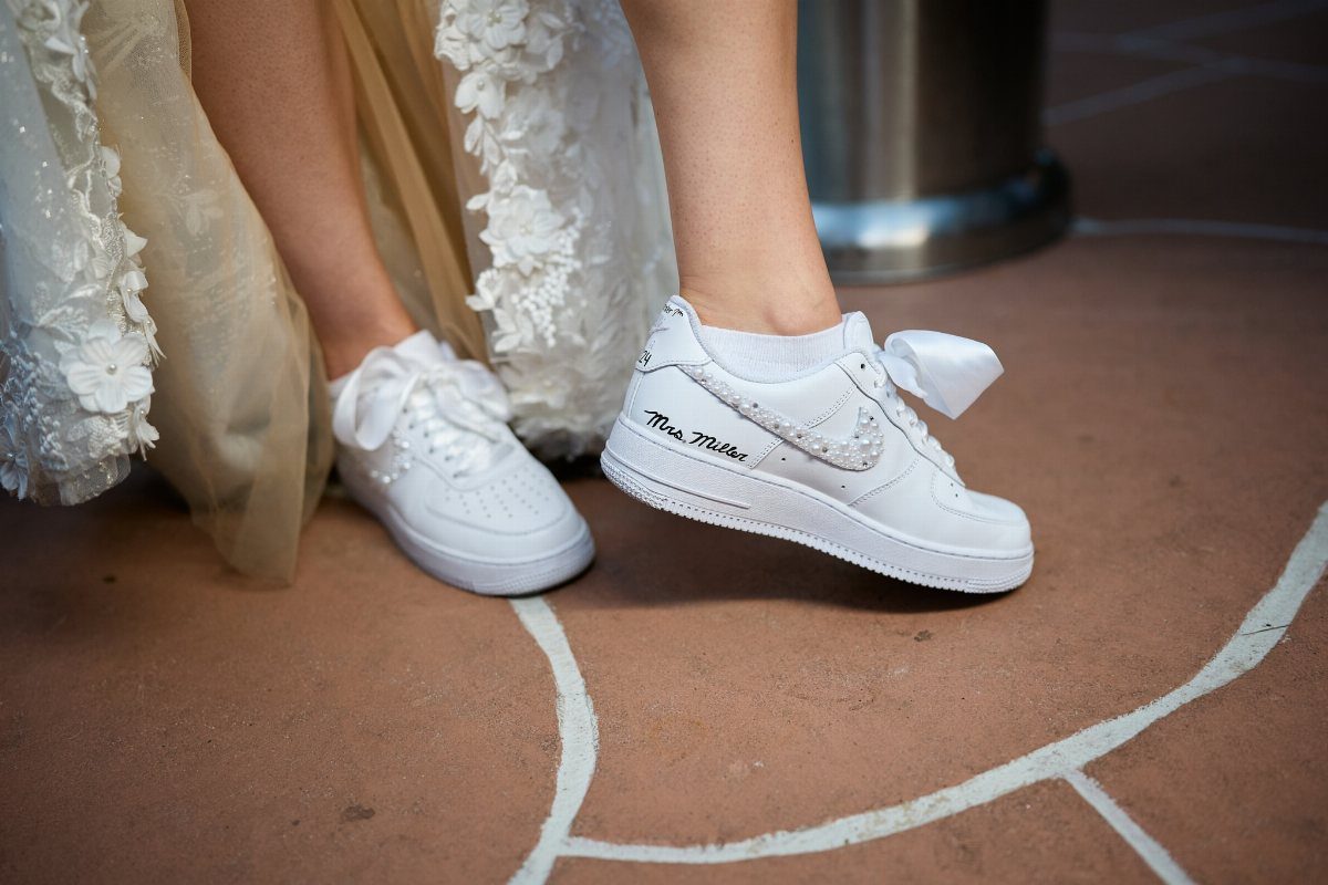 White Nike sneakers with bows worn with a white lace wedding dress.