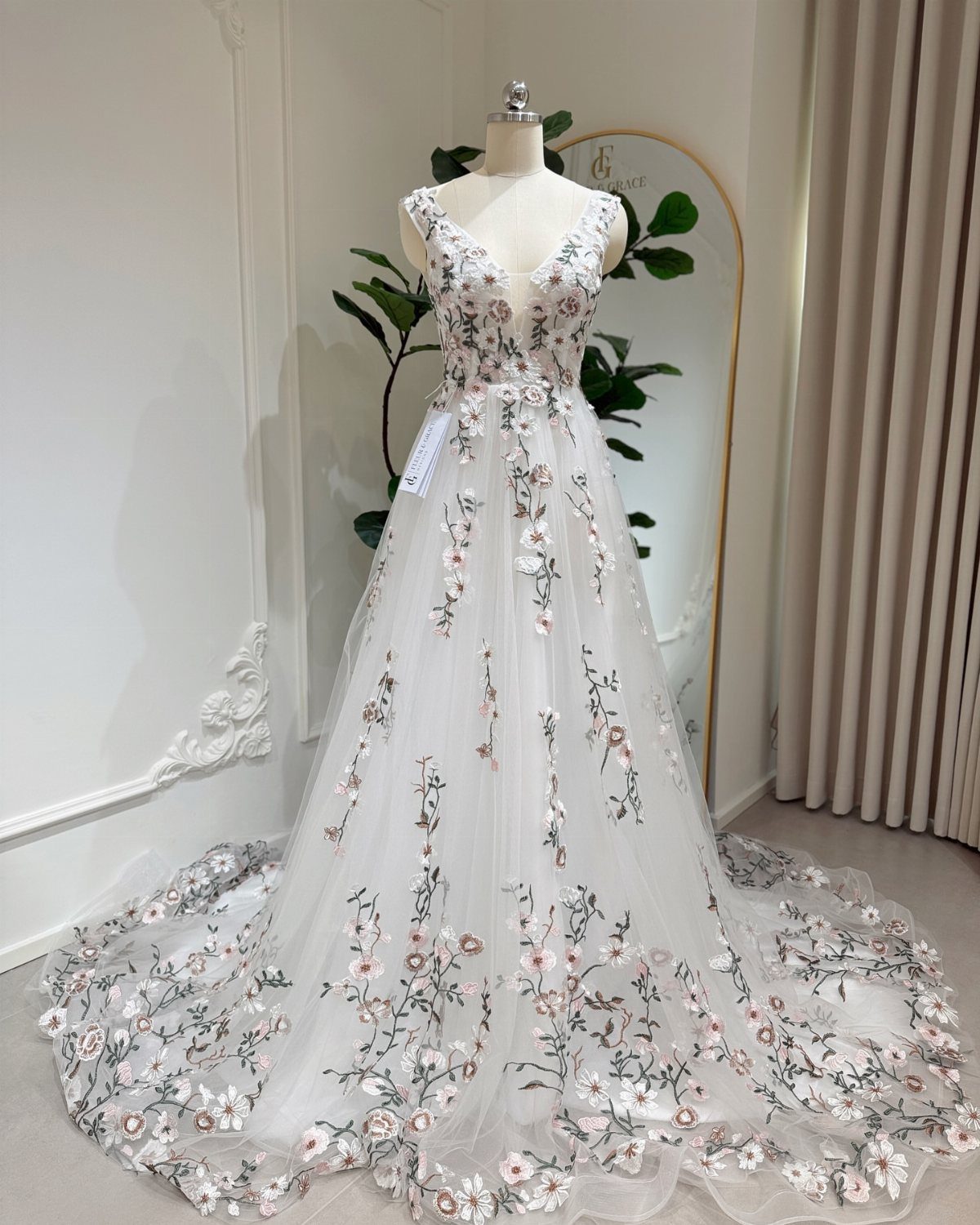 White wedding gown with pink floral embroidery on a mannequin in a bright room