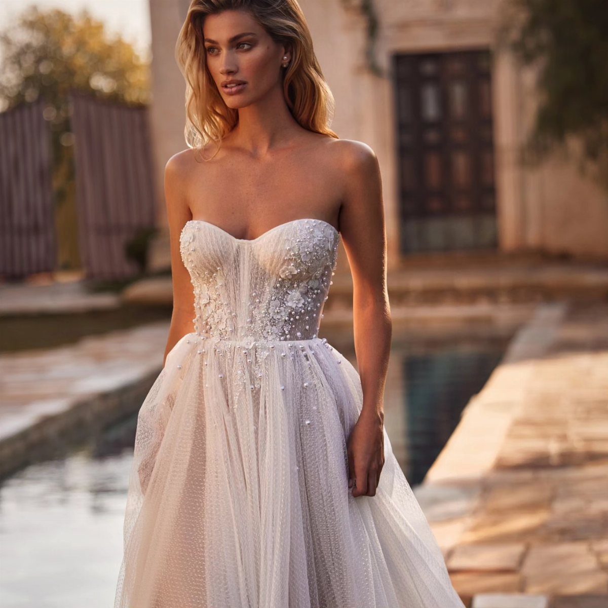 Woman in a strapless white wedding dress with floral bodice and tulle skirt outdoors.