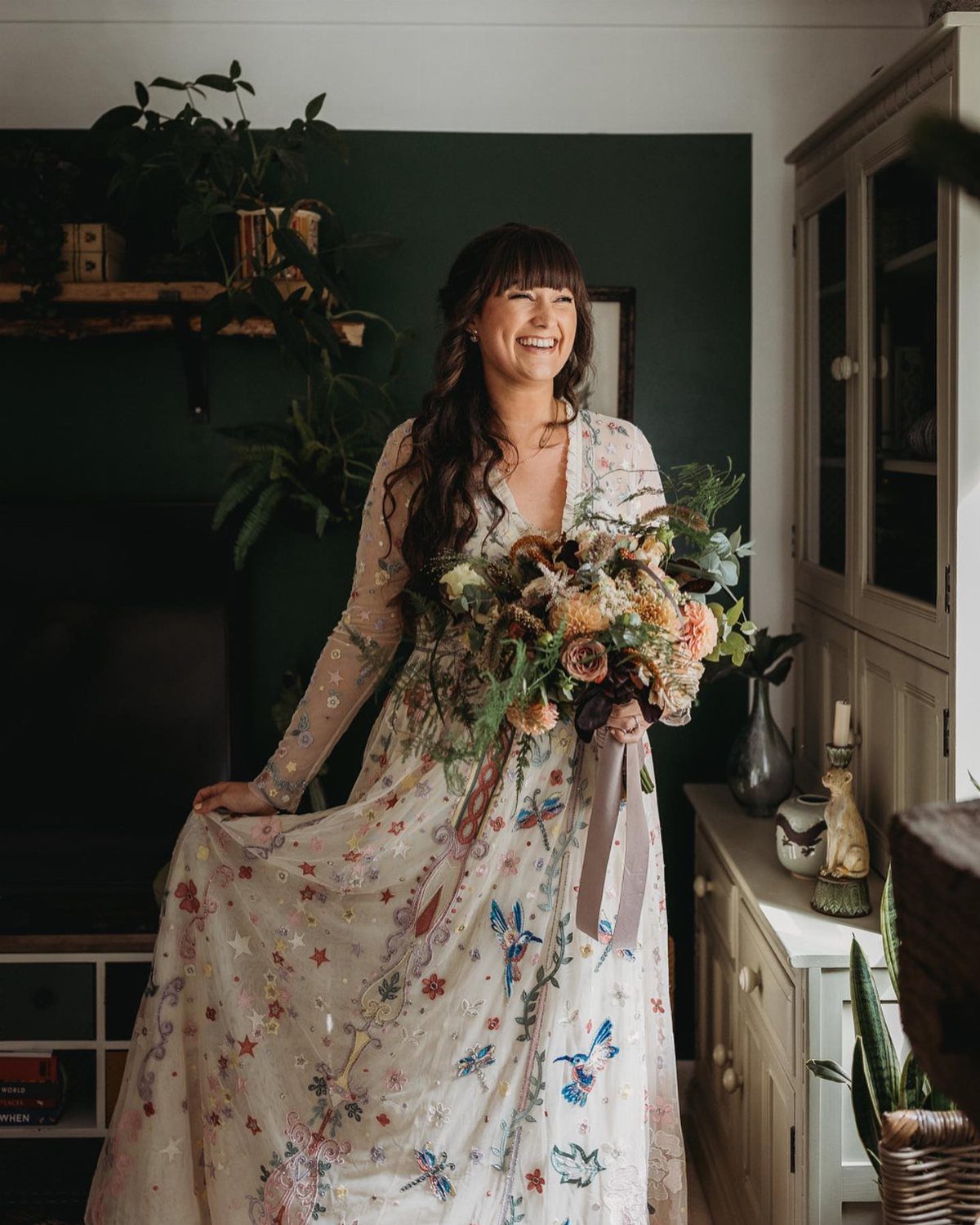 Woman in a long-sleeved floral wedding dress holding a colorful wildflower bouquet.