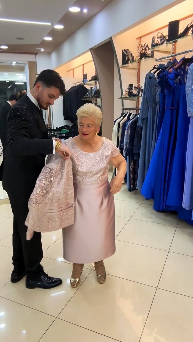 Older woman wearing a light pink lace and satin dress in a clothing store.