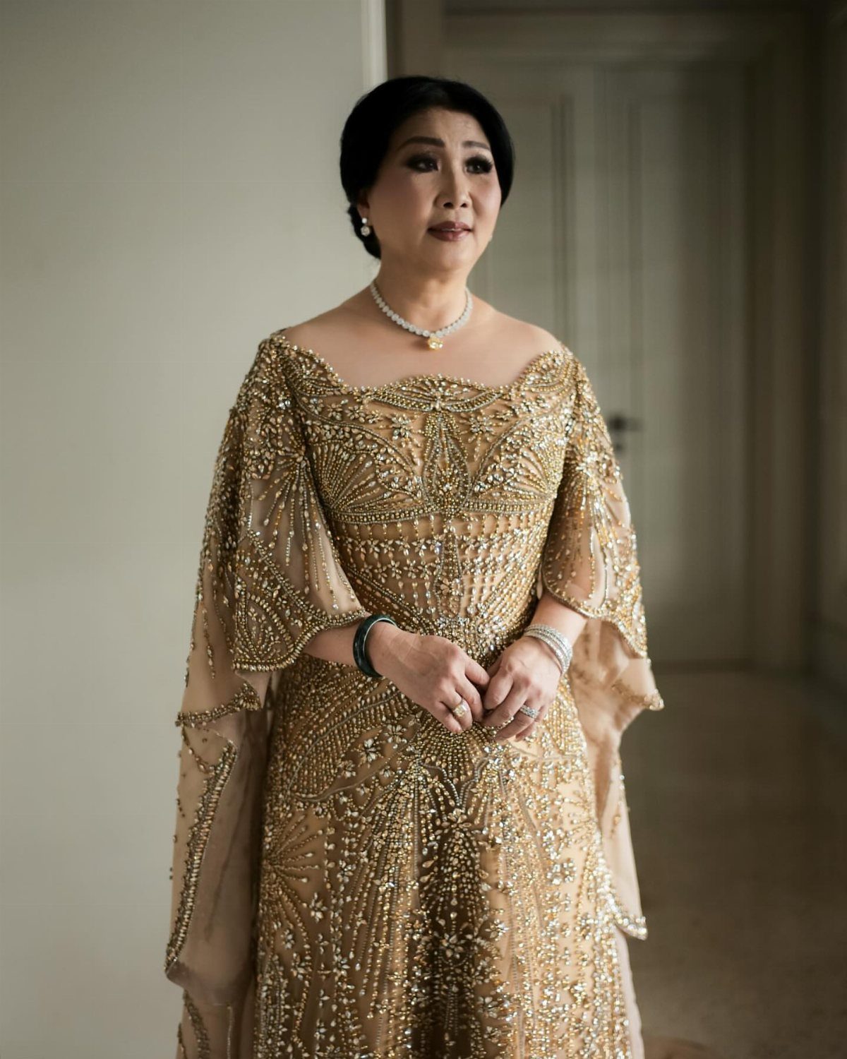 Older woman in a gold embellished floor-length gown with a matching cape.