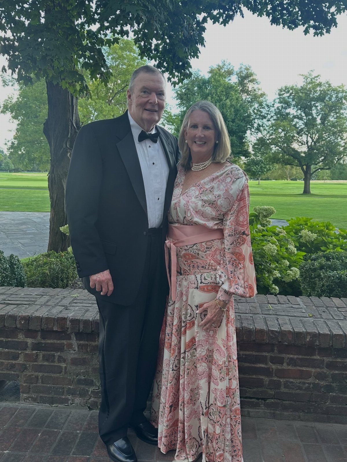 Couple posing outdoors, woman wearing a peach paisley long dress and man in tuxedo.