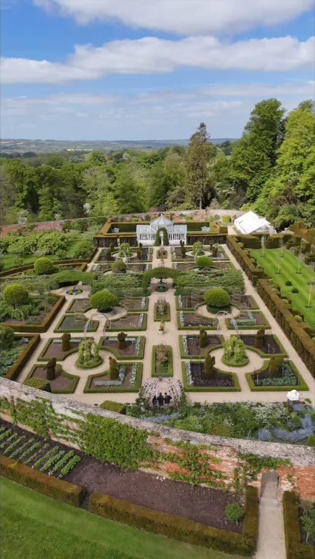 Formal garden with symmetrical hedges and a white glass greenhouse at the end.