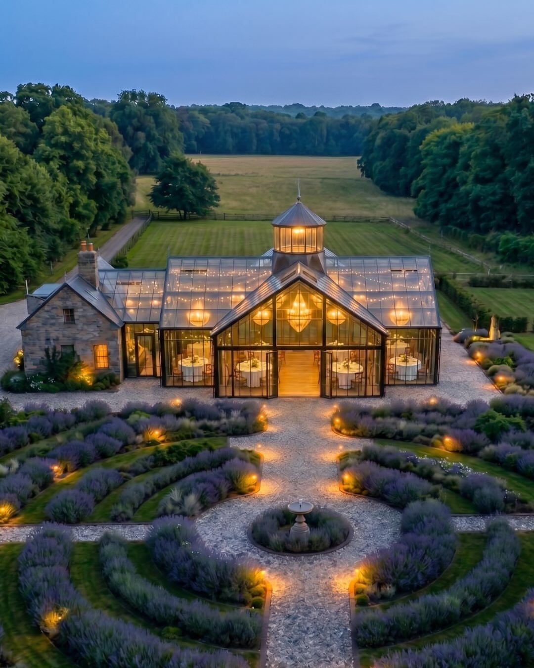 Glass conservatory wedding venue surrounded by illuminated lavender gardens at dusk