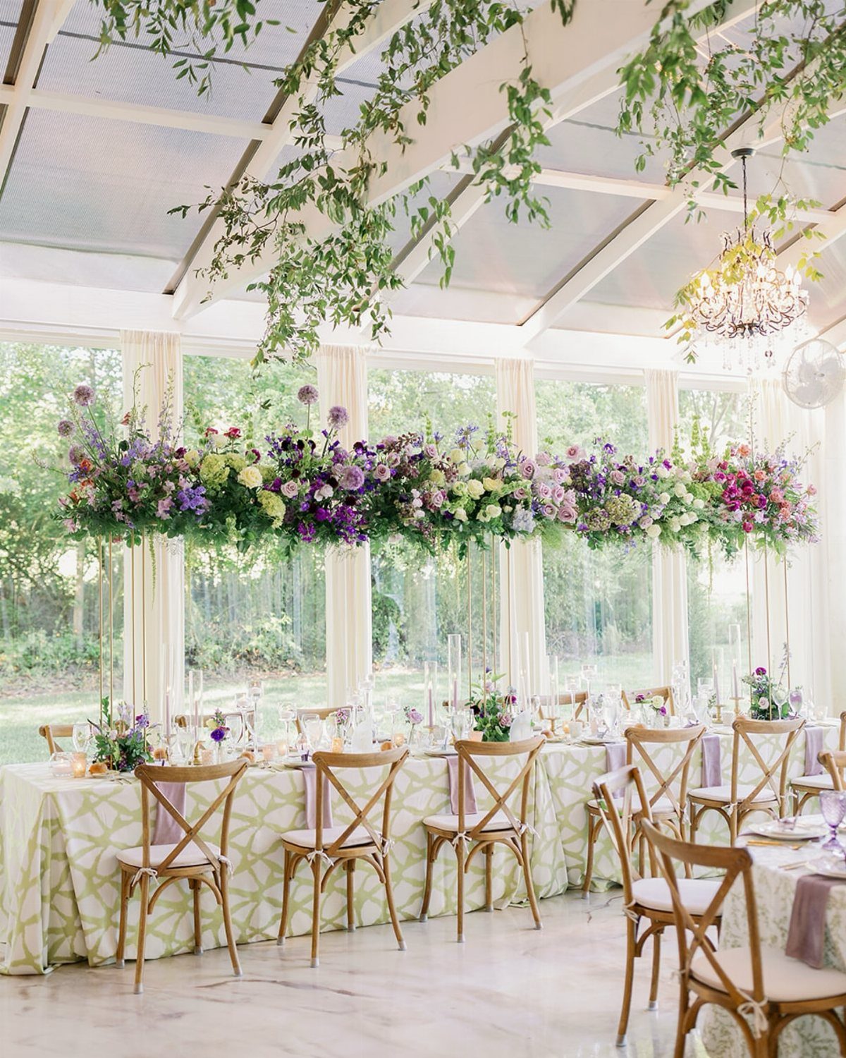 Wedding reception table with lush floral runner inside a bright glasshouse greenhouse venue.