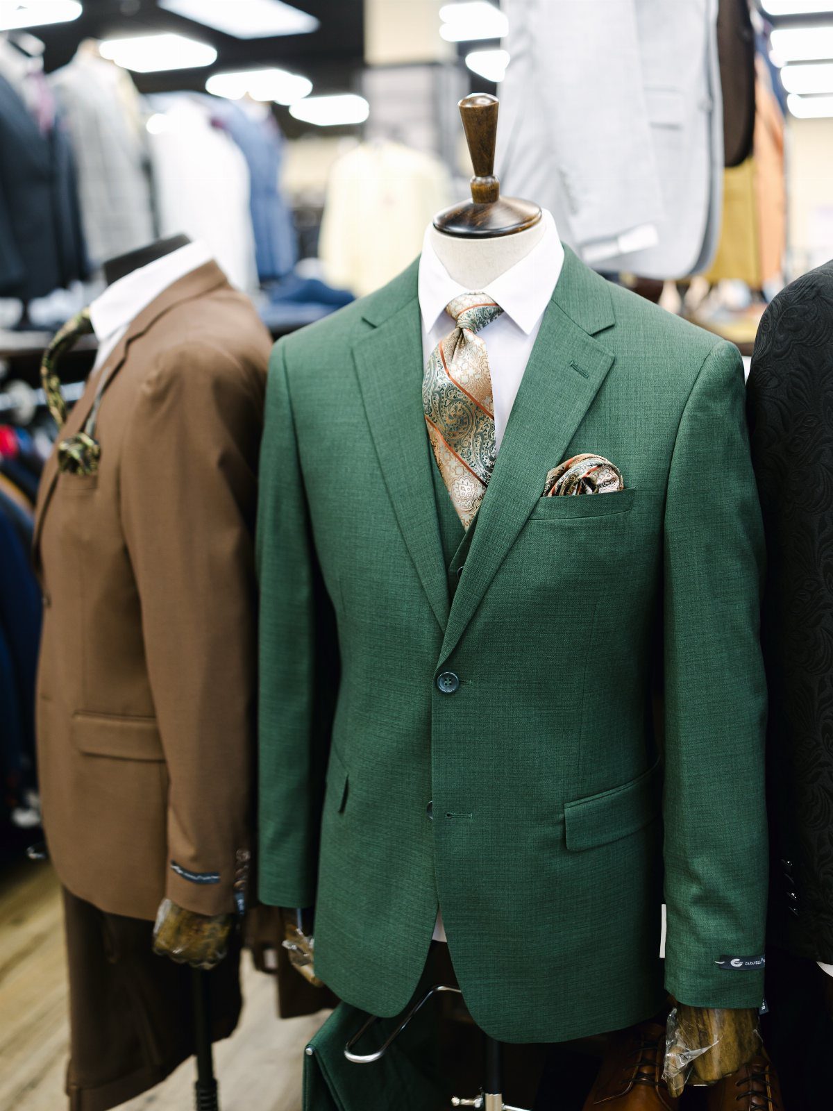 Green three-piece suit on a mannequin with a patterned tie and pocket square.