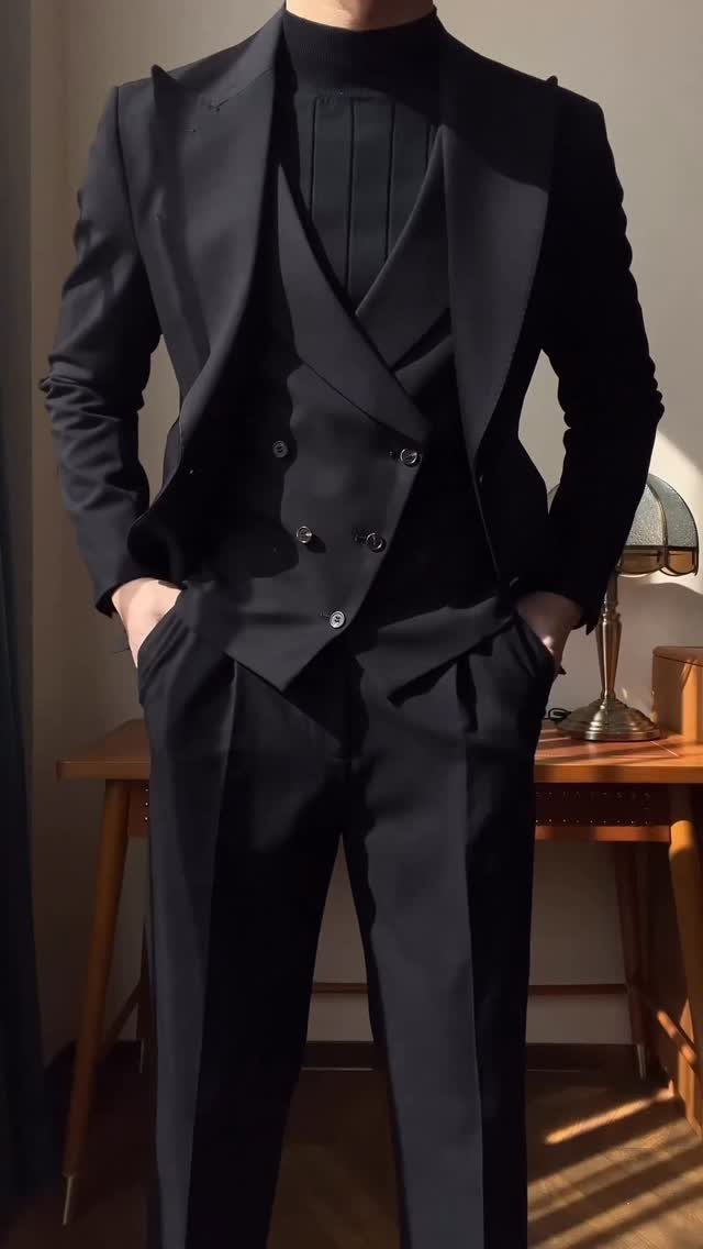 Man in a black three-piece suit with a black turtleneck standing indoors.