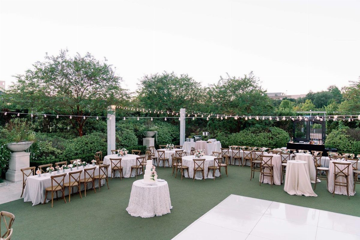 Outdoor wedding reception with white tables, wooden chairs, and string lights on green turf.