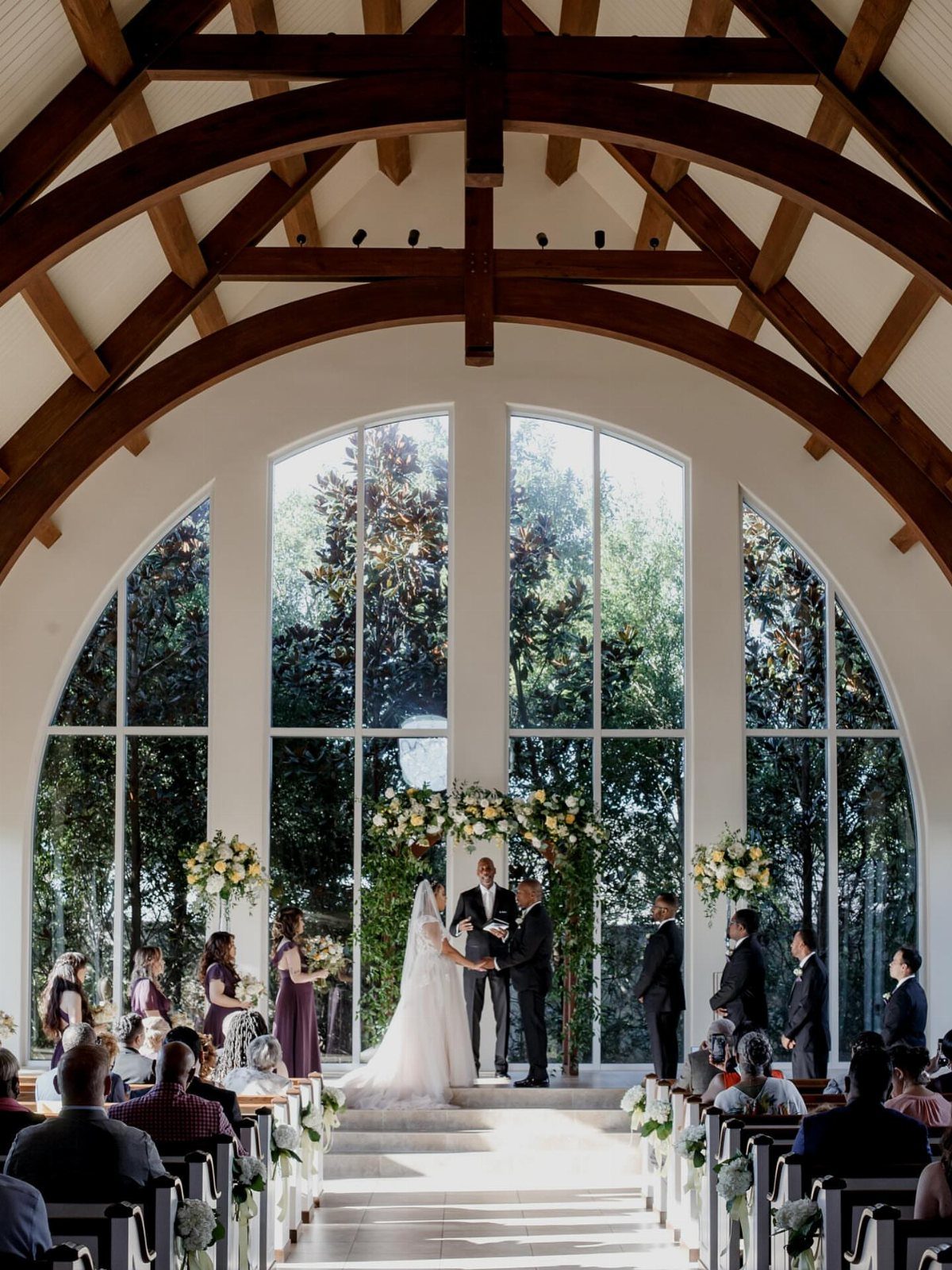 Wedding ceremony in a bright hall with vaulted wooden beams and large arched windows.