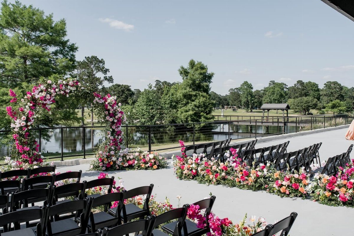 Outdoor wedding ceremony setup with floral arch and chairs overlooking a pond and trees.
