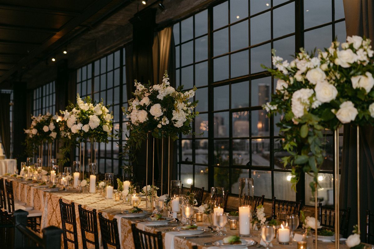 Wedding reception table with white flowers and candles before large glass walls overlooking skyline