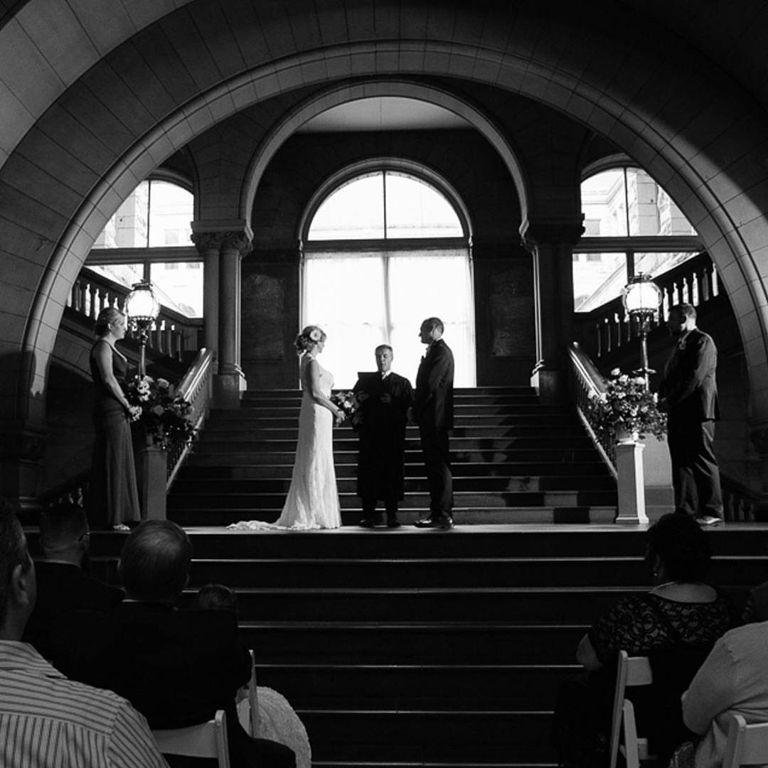 Wedding ceremony on a grand stone staircase under a large architectural archway.
