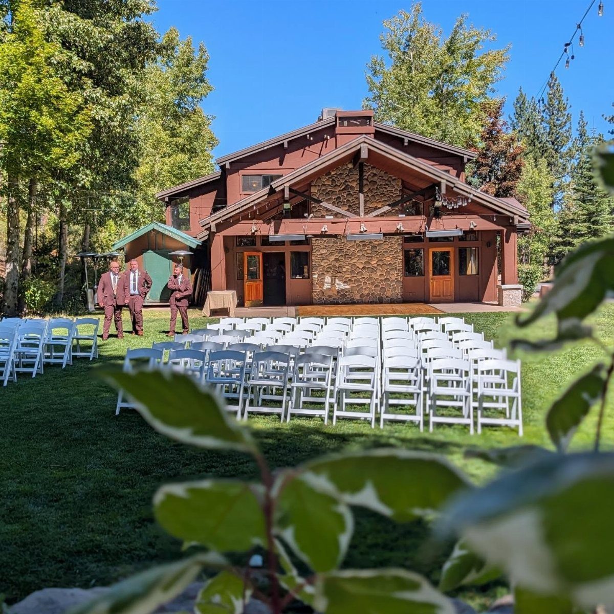 White wedding chairs on a lawn before a rustic brown wooden lodge.