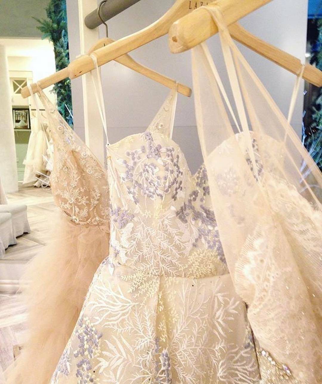 Intricate wedding dresses with floral embroidery hanging on wooden hangers in a boutique.