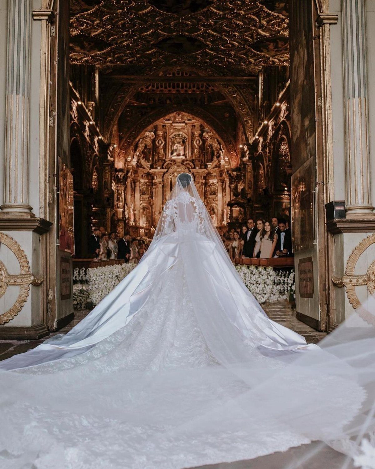 Bride in a white lace wedding gown with a long train in a church.