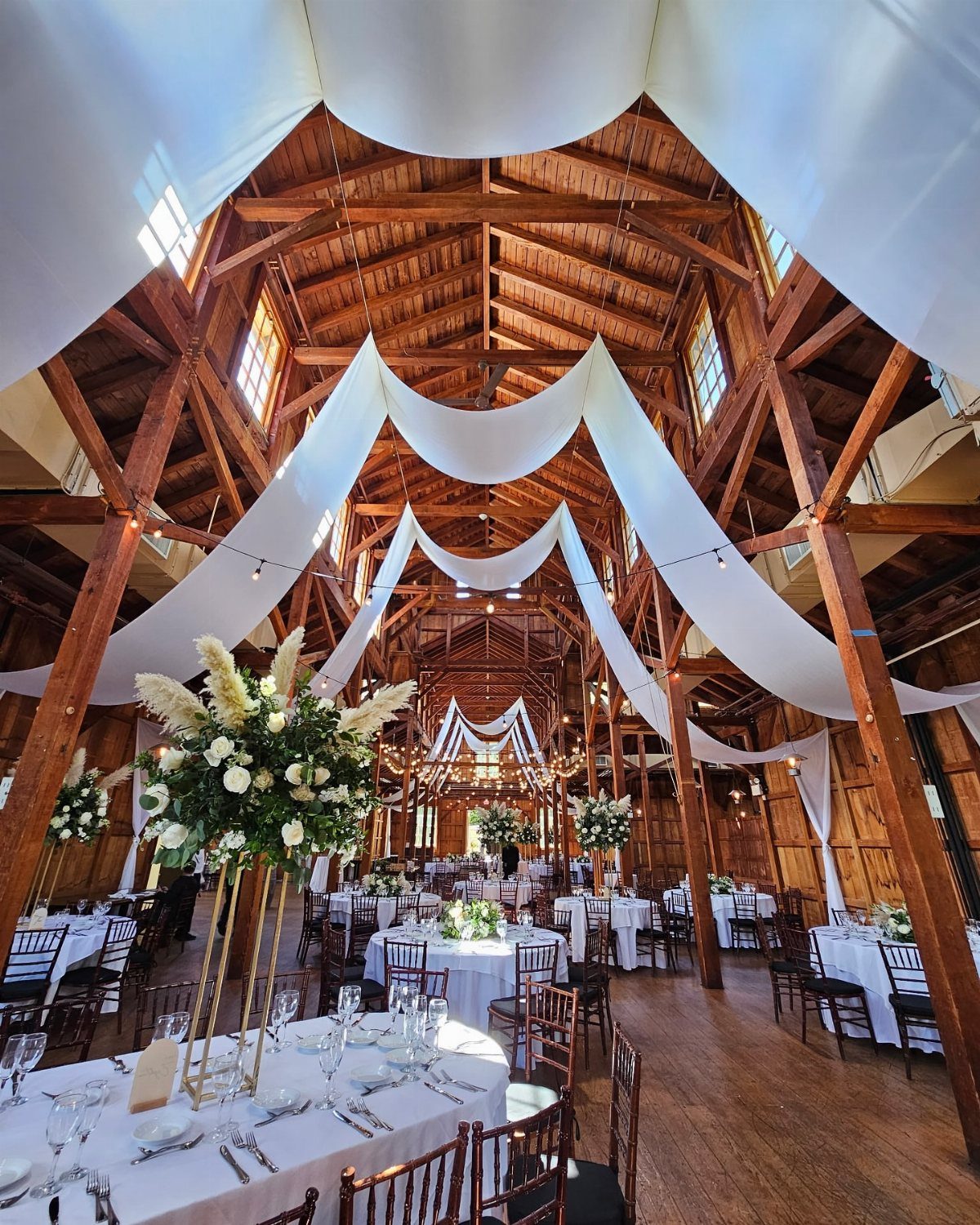 Rustic wooden barn interior decorated with white fabric drapes and elegant wedding tables.