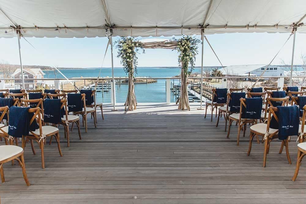 Wedding ceremony setup on a wooden deck overlooking a nautical bay with docks.