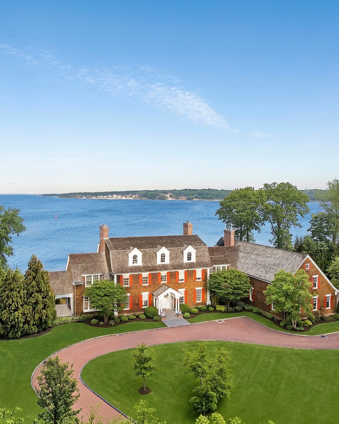 Large red brick waterfront mansion with a curved driveway and manicured green lawns.