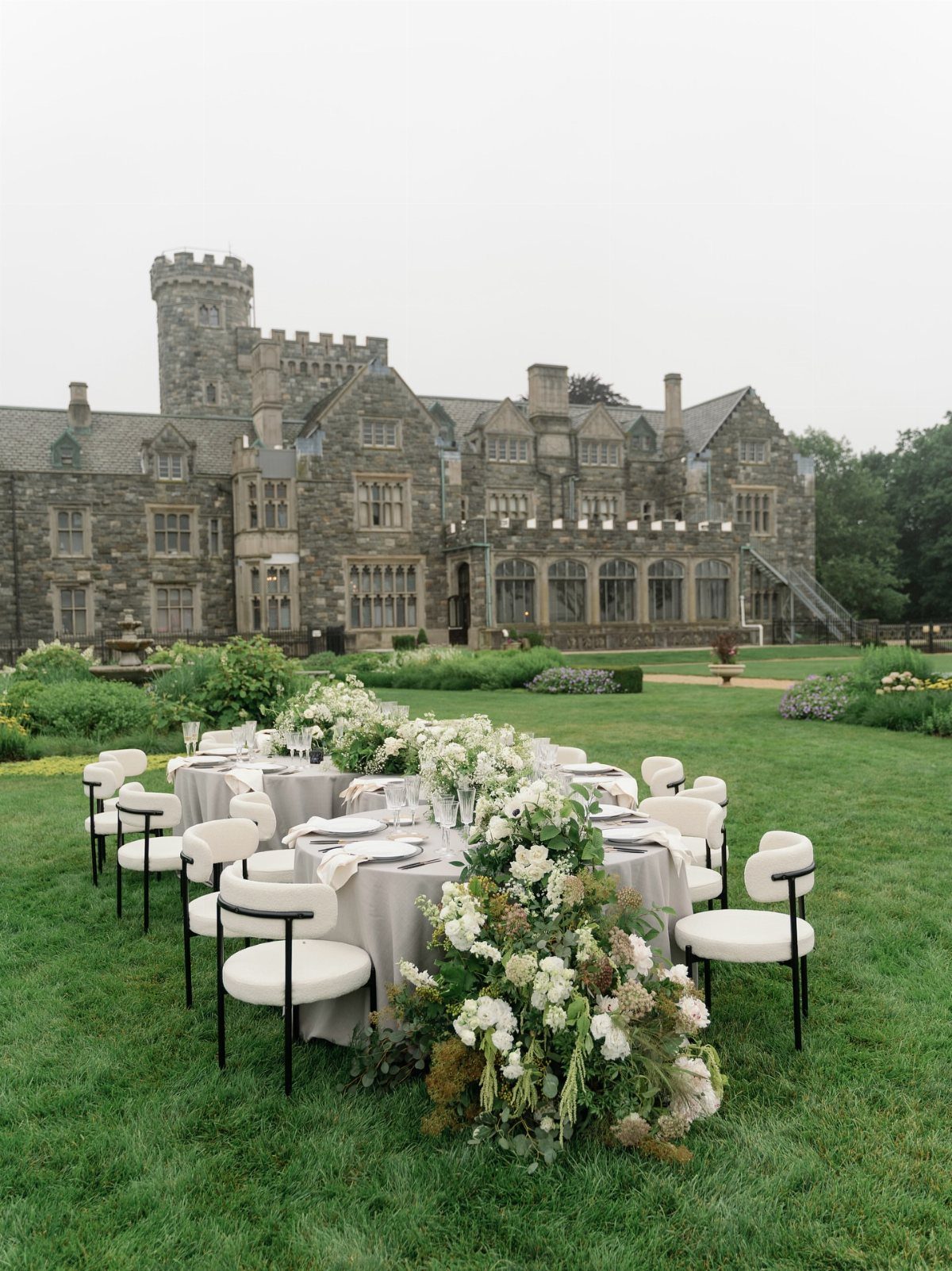 Wedding reception table with white flowers on a lawn before a stone estate.