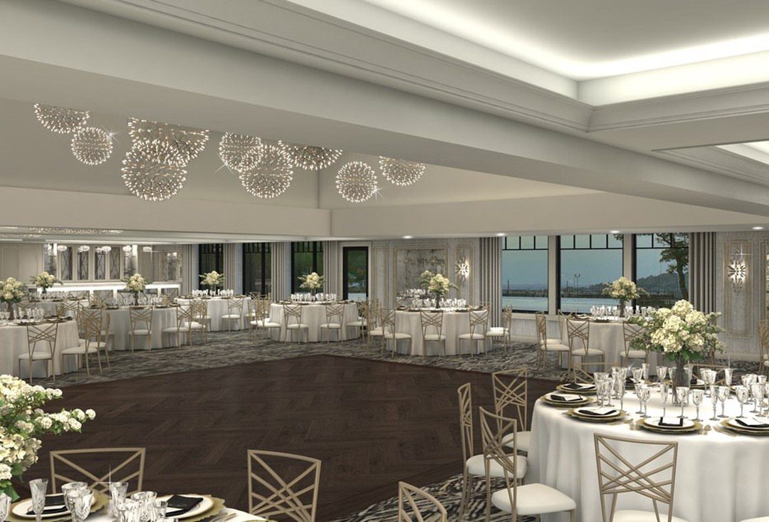 Luxury waterfront ballroom with white tables, floral centerpieces, and modern spherical chandeliers.