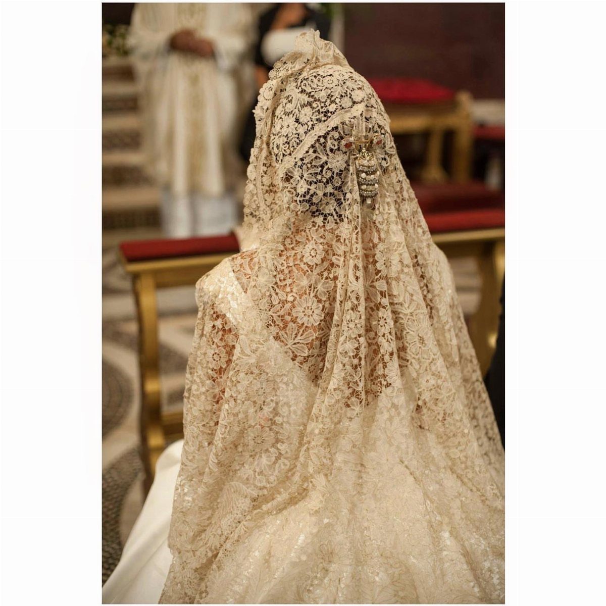Woman wearing a long ivory lace mantilla wedding veil in a church setting.