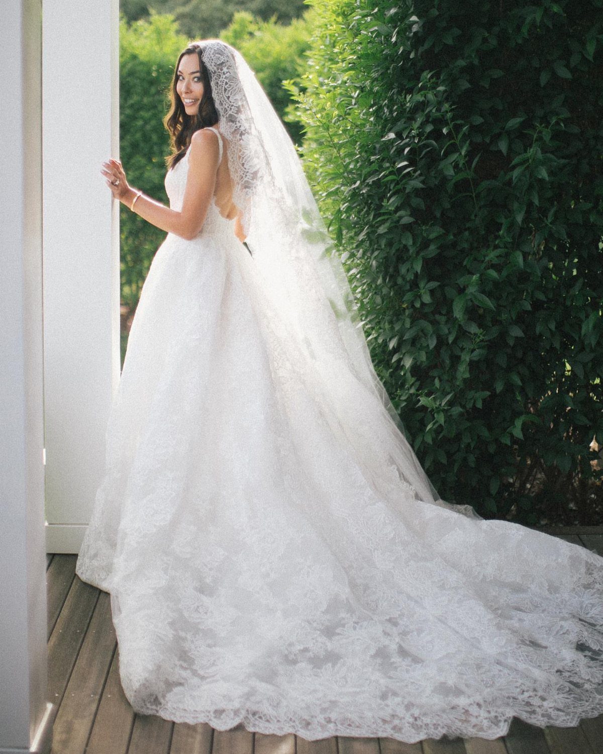 Bride wearing a long white lace mantilla wedding veil on a wooden deck