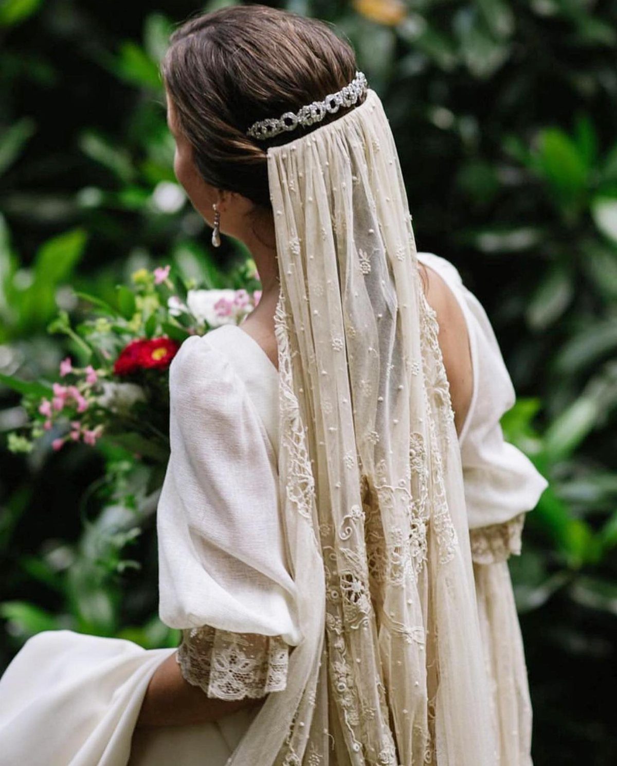 Bride from behind wearing a lace mantilla veil and sparkling tiara in a garden