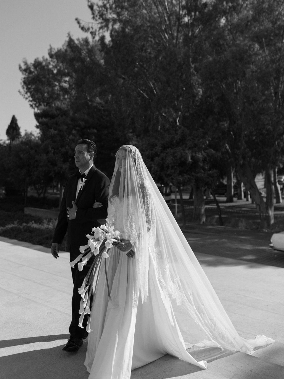 Bride wearing a traditional lace-edged mantilla wedding veil walking with her groom.
