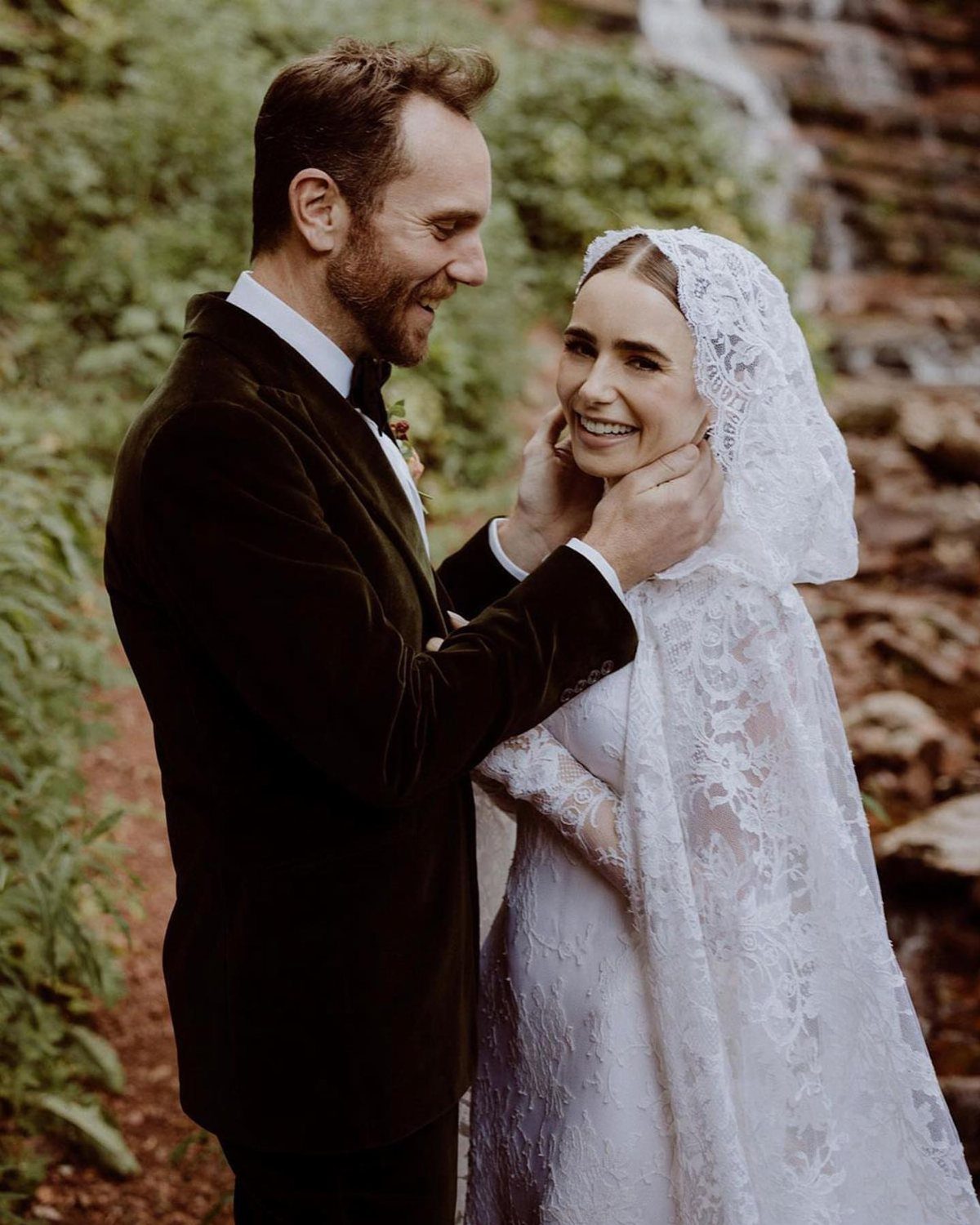 Bride in a lace mantilla veil and groom in velvet tuxedo by a waterfall.