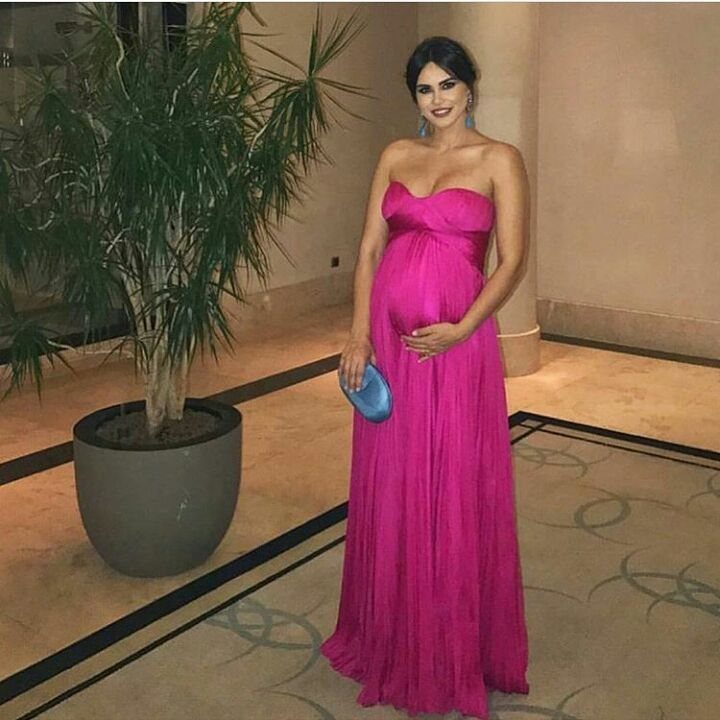Pregnant woman in a strapless bright pink floor-length gown holding a blue clutch.